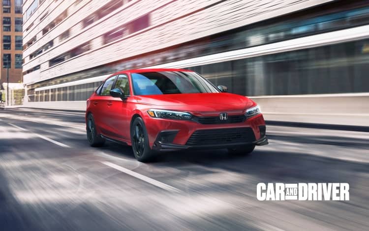 Front driver-side view of the 2022 Honda Civic Sport Sedan in Rallye Red, driving on a city street.