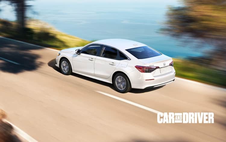 Front passenger-side three-quarter view of the 2021 Honda Civic Sport Sedan in Rallye Red driving through a city center. 