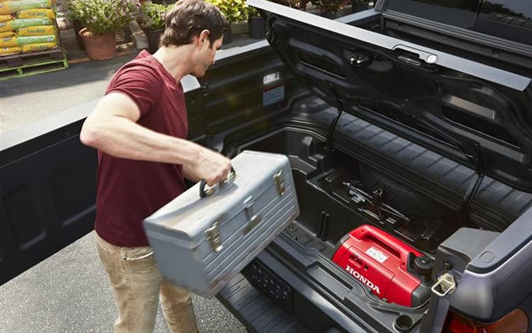 2026 Ridgeline RTL in Modern Steel Metallic Slight overhead shot of truck bed with tailgate opening, and a person is accessing locking in bed trunk with prop