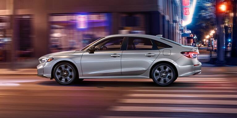 2027 Honda Civic Sedan Sport Touring Hybrid in Solar Silver Metallic side profile driving on a city street (Compact Sedan)